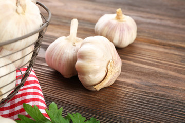 Fresh garlic in the basket decorated with parsley and red checkered cotton napkin on wooden background, close up