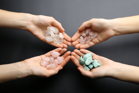 Women holding semiprecious stones in their hands on dark grey background