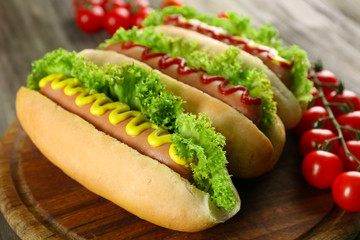 Tasty hot-dogs with tomatoes on wooden background