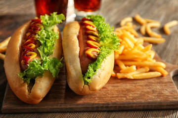 Delicious hot-dogs with French fries on wooden chopping board, close up