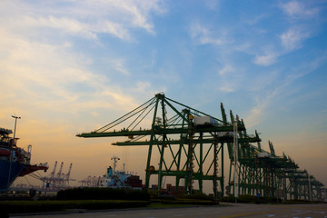 View of cranes and cargo ships at dusk