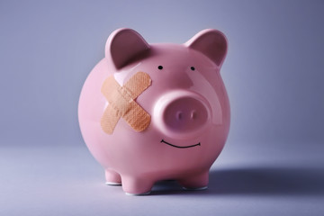 Piggy Bank with adhesive bandage on grey background
