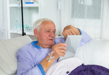 Older man receives infusion and uses a digital tablet