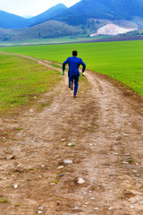 groom in blue suit running away with beer bottles on a field path.