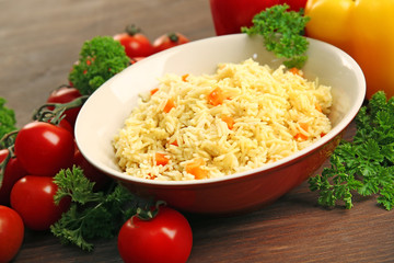 Stewed rice with a carrot on a plate over wooden background
