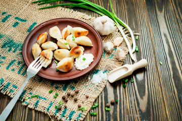 Ukrainian and china national cuisine , fried dumplings with meat or potatoes with sour cream or mayonnaise , green onions, garlic , pepper and spices on a wooden background