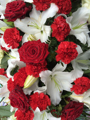 Beautiful pretty floral tribute of red roses, carnations and white lilies. With rain or dew drops on the petals. 