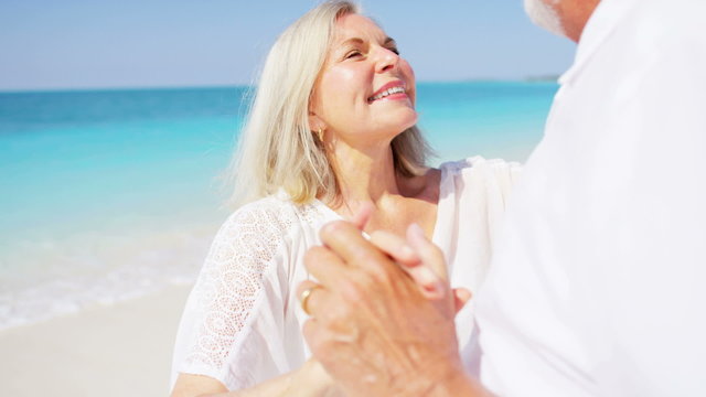 Senior Caucasian couple in white dancing together on a Caribbean beach