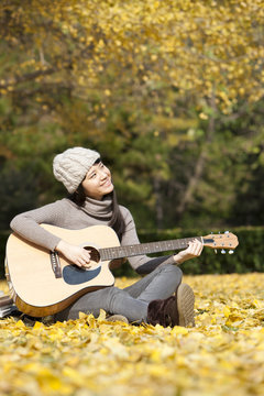 Lovely female college student with guitar enjoying the beautiful autumn on campus