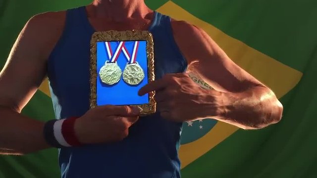 Athlete choosing gold medals on his tablet standing against Brazilian flag