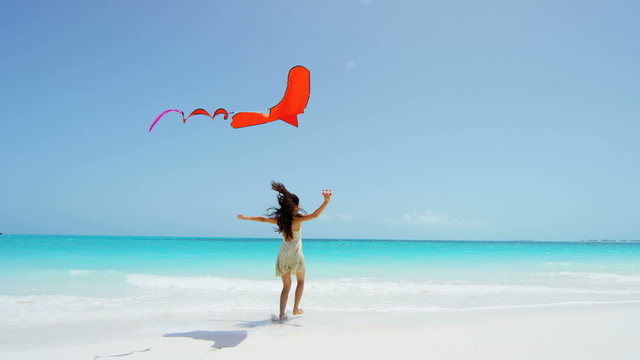Laughing Asian Chinese girl with red kite enjoying tropical beach