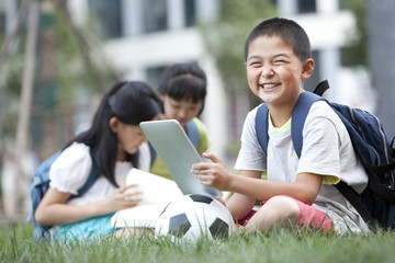 Schoolchildren sitting on the lawn with digital tablet