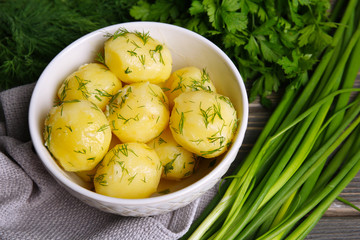 Boiled potatoes with greens in bowl on table close up