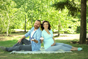 Beautiful pregnant woman with her beloved husband with baby booties in the park