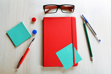 Red notebook with stationery on wooden background
