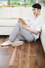 Cheerful young man reading book in living room