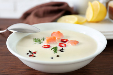 Delicious salmon cream soup with spoon on wooden table, close up