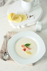 Delicious cream soup with fish and sliced lemon on white table in the restaurant