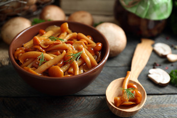 Delicious marinated mushrooms in bowl on wooden background