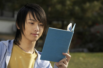 Fototapeta premium Young Man Sitting On Park Bench Reading Book