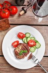 Roasted beef fillet and fresh vegetables on plate, on wooden background