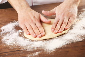 Hands preparing dough basis for pizza on the wooden table, close-up