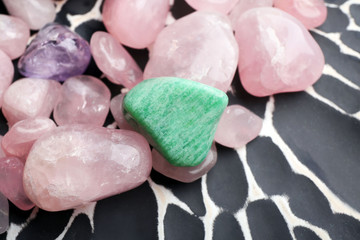 Naklejka premium Rose quartz, aventurine, and amethyst tumbled stones on black and white patterned surface, healing crystals and gemstones