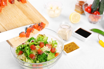 Female hands adding pieces of salmon into bowl with salad, close-up