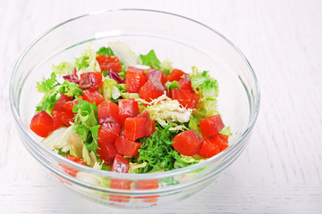 Tasty salad in glass dish on color wooden table background