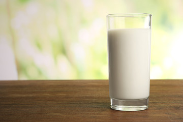 Glass of milk on table on blurred natural background