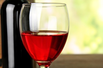 Wine in glass and in bottle on blurred natural background closeup