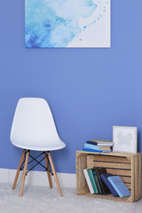 Room design with white chair, bookcase and picture over blue wall