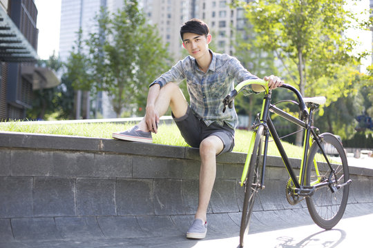 Portrait of happy young man holding bicycle while sitting outdoors