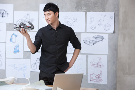 Car designer holding model car in studio