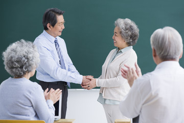 Senior student having a handshake with teacher in classroom