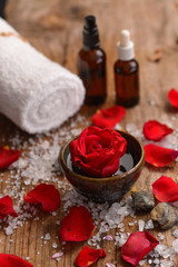 roses in bowl with pile of salt ,stones ,oil,towel,candle on old wooden board