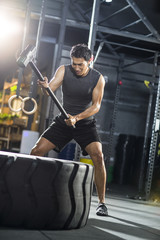 Fototapeta na wymiar Young man hammering large tire at gym