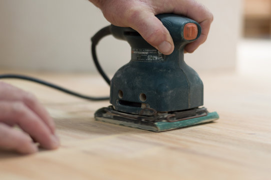 Close up of a man's hands and sander sanding a wood floor 