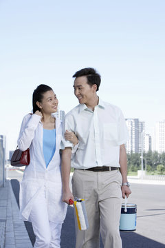 Man And Woman Linking Arms, Walking And Smiling At Each Other