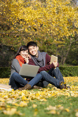 Sweet college couple with laptop and books enjoying the scenic autumn on campus