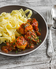 Chicken meatballs in tomato sauce and fettuccine pasta in a brown bowl on bright wooden surface.
