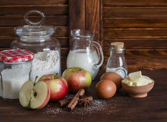 Ingredients and tools for baking - flour, eggs, butter, apples, cinnamon on a brown rustic wooden surface.  Ingredients for baking apple pie