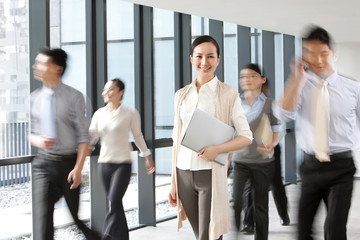 Businesswoman in hallway with blurred business people walking around her