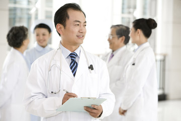 Fototapeta premium Doctor in Forground with Clipboard, Doctors and a Nurse in Background