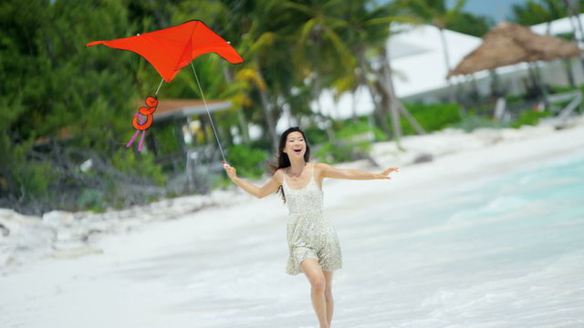 Smiling Asian Chinese girl playing with red kite on beach 