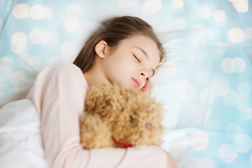 girl sleeping with teddy bear toy in bed