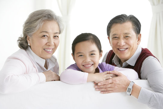Chinese grandparents and gradaughter turning around and smiling on the living room sofa