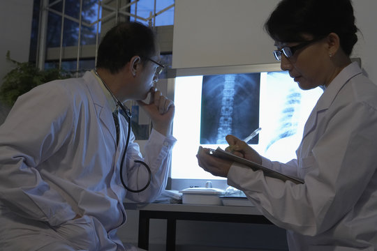 Male doctor examining x-ray on monitor while female doctor taking note