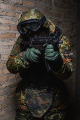 Fototapeta premium Armed man in helmet and body armor/ Armed man in helmet, body armor, mask, with weapon in hand takes aim at target