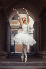 Naklejka premium Looks like she is going to fly. Beautiful young female ballet dancer practicing her poses in an archway outdoors soft focus